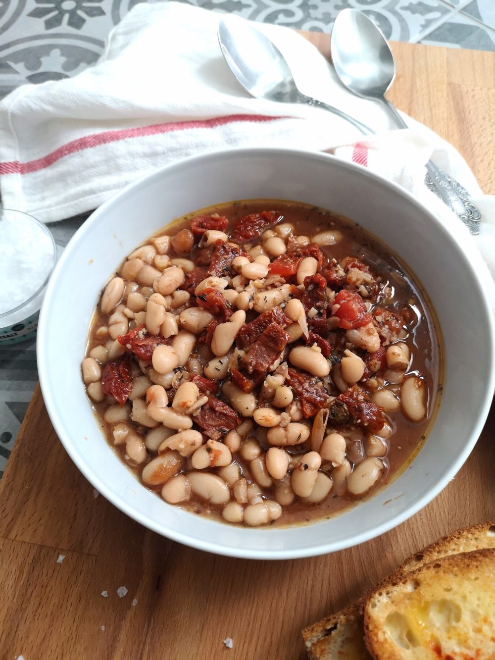 beans soup in a white dish on a table next to bread slices