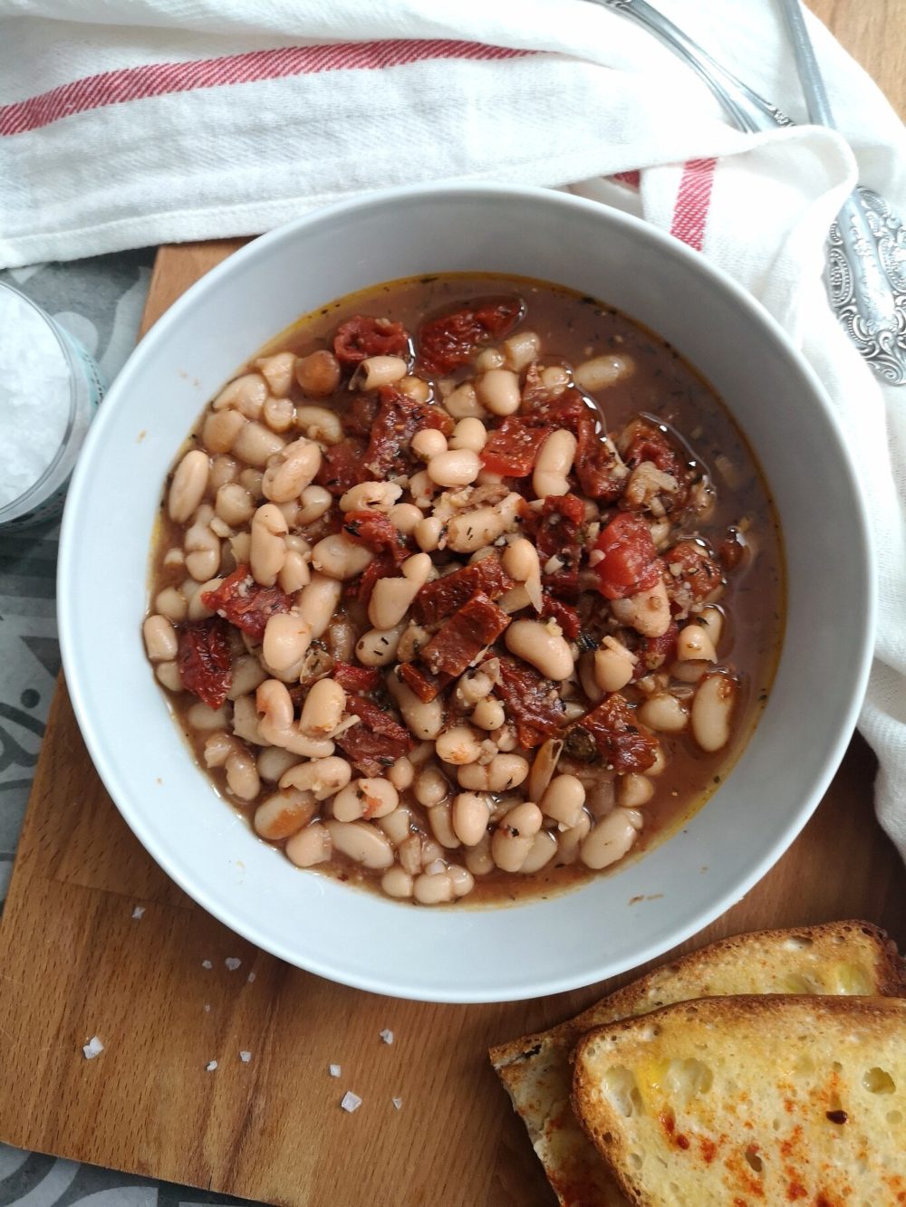 beans soup in a white dish on a table next to bread slices