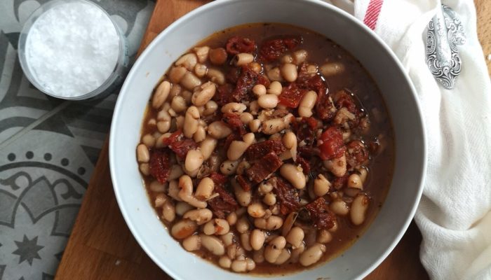 beans soup in a white dish on a table next to bread slices