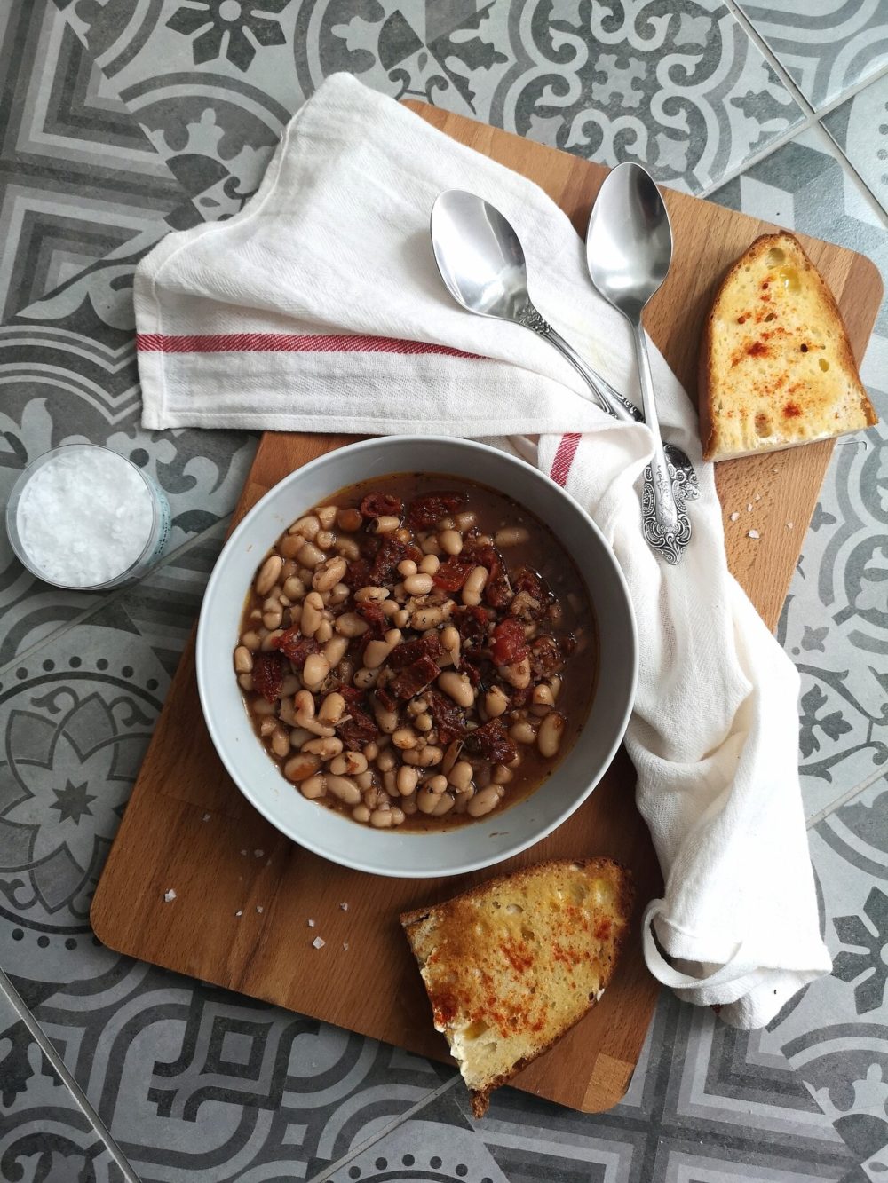 beans soup in a white dish on a table next to bread slices