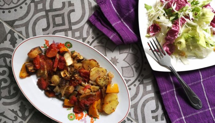 vegan briam (vegetable bake) on a white dish with a fork next to salad on a plate