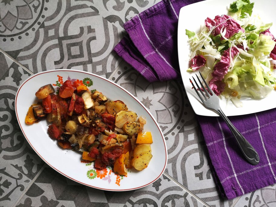 vegan briam (vegetable bake) on a white dish with a fork next to salad on a plate