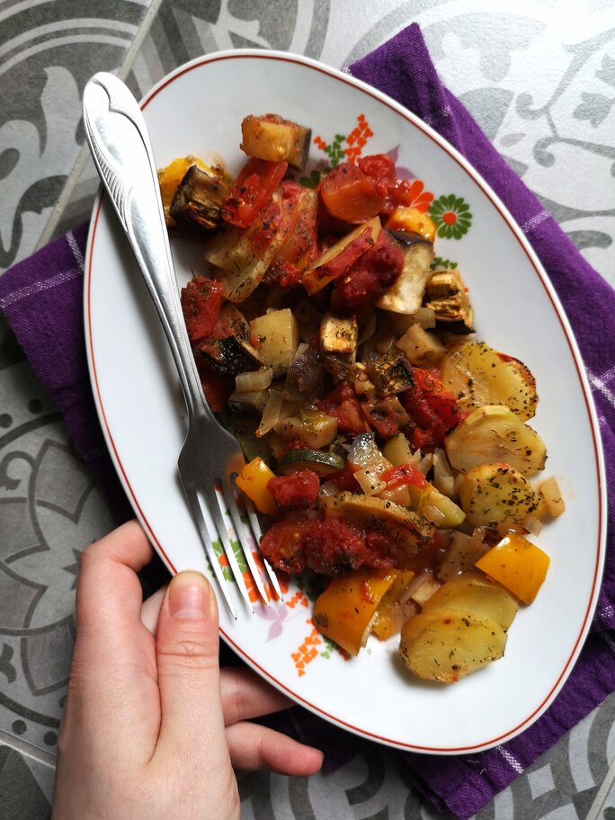 vegan briam (vegetable bake) on a white dish with a fork