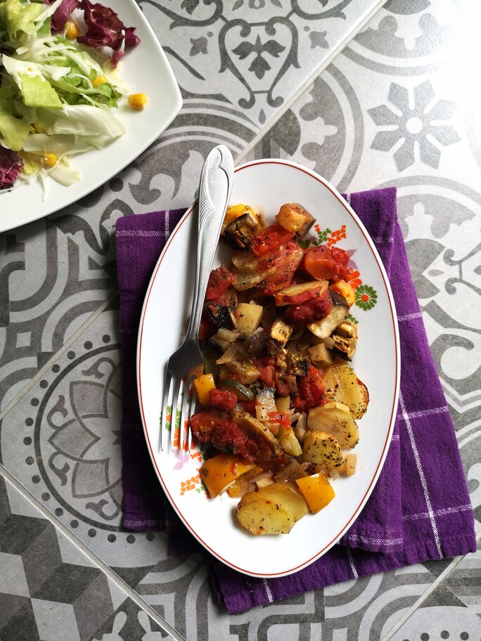vegan briam (vegetable bake) on a white dish with a fork