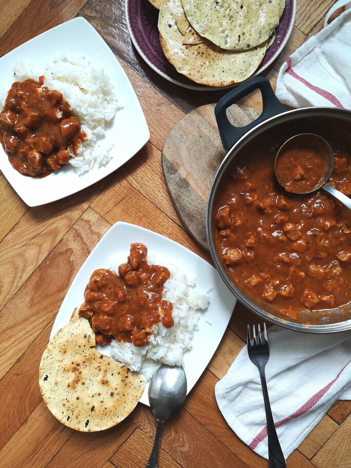vegan kashmiri rogan josh in a pot and on a plate with white rice on a table