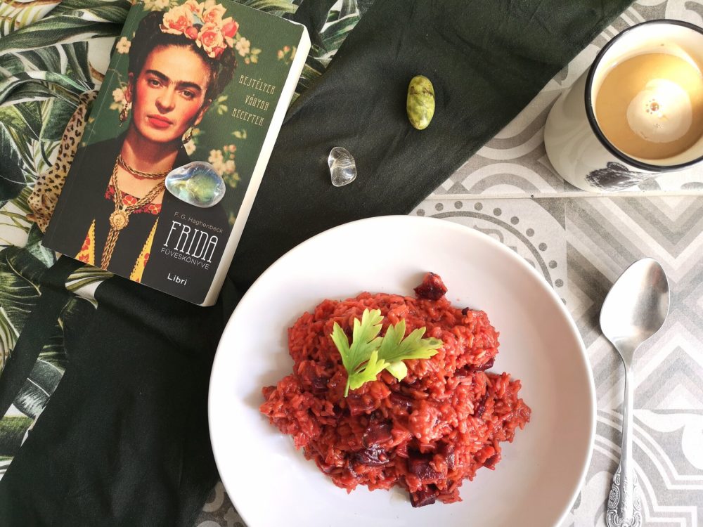 beet risotto on a white plate next to a spoon, coffee cup, and book