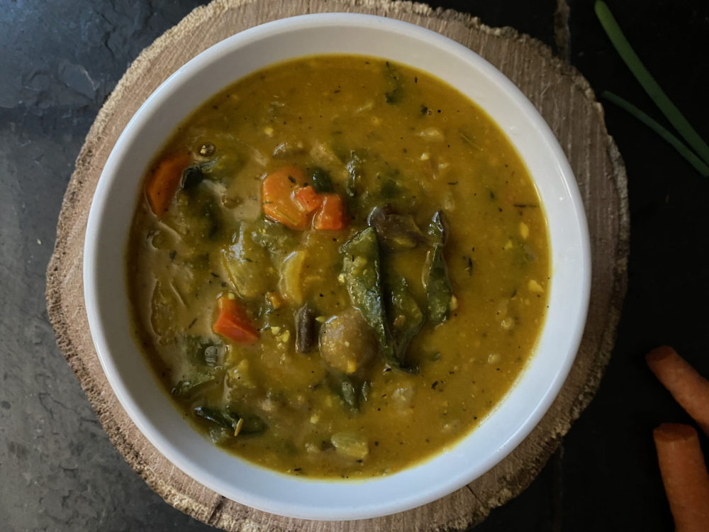 vegan haitian pumpkin soup in a white bowl against a brown and black background