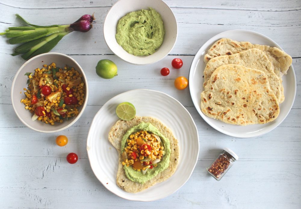 flatbread with charred corn and green hummus on white plates against a white tabletop