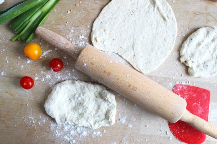 dough for flatbread with a rolling pin and vegetables