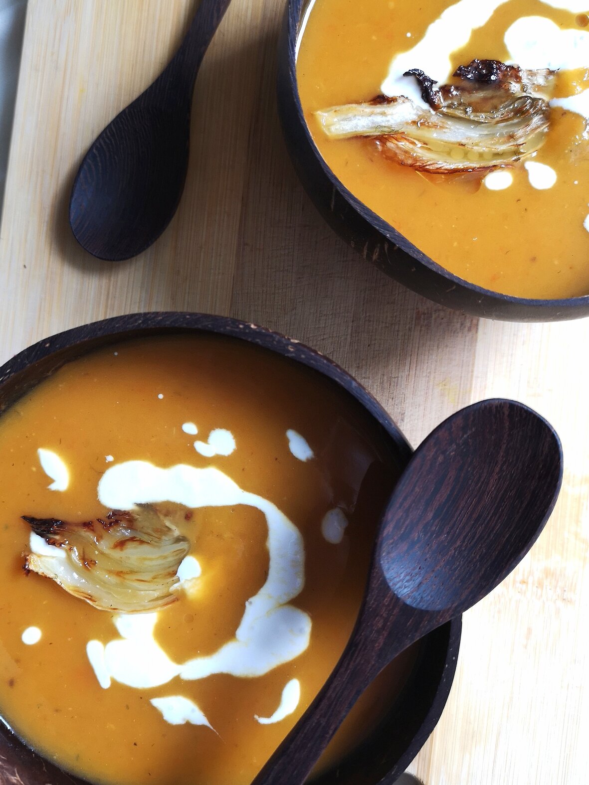 vegan creamy roasted carrot, sweet potato, and fennel soup in two bowls on a cutting board with spoons