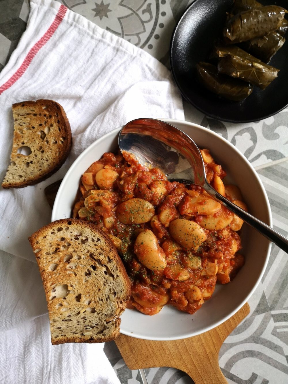 gigantes beans in a white bowl with bread and a silver spoon