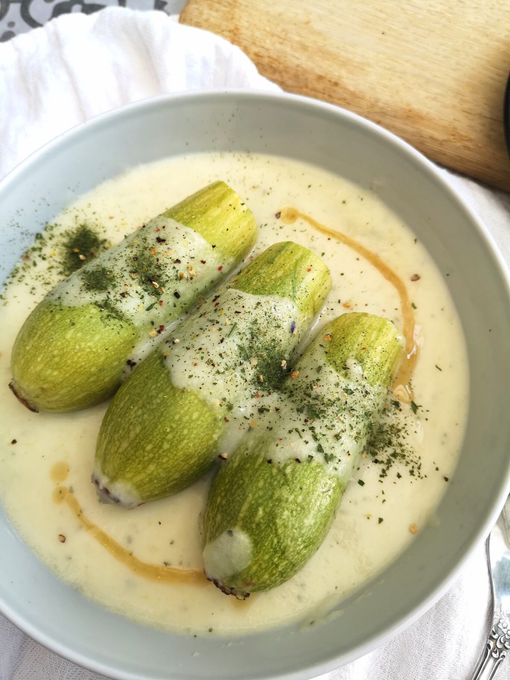 vegan stuffed zucchini in yogurt sauce in a white bowl with a spoon