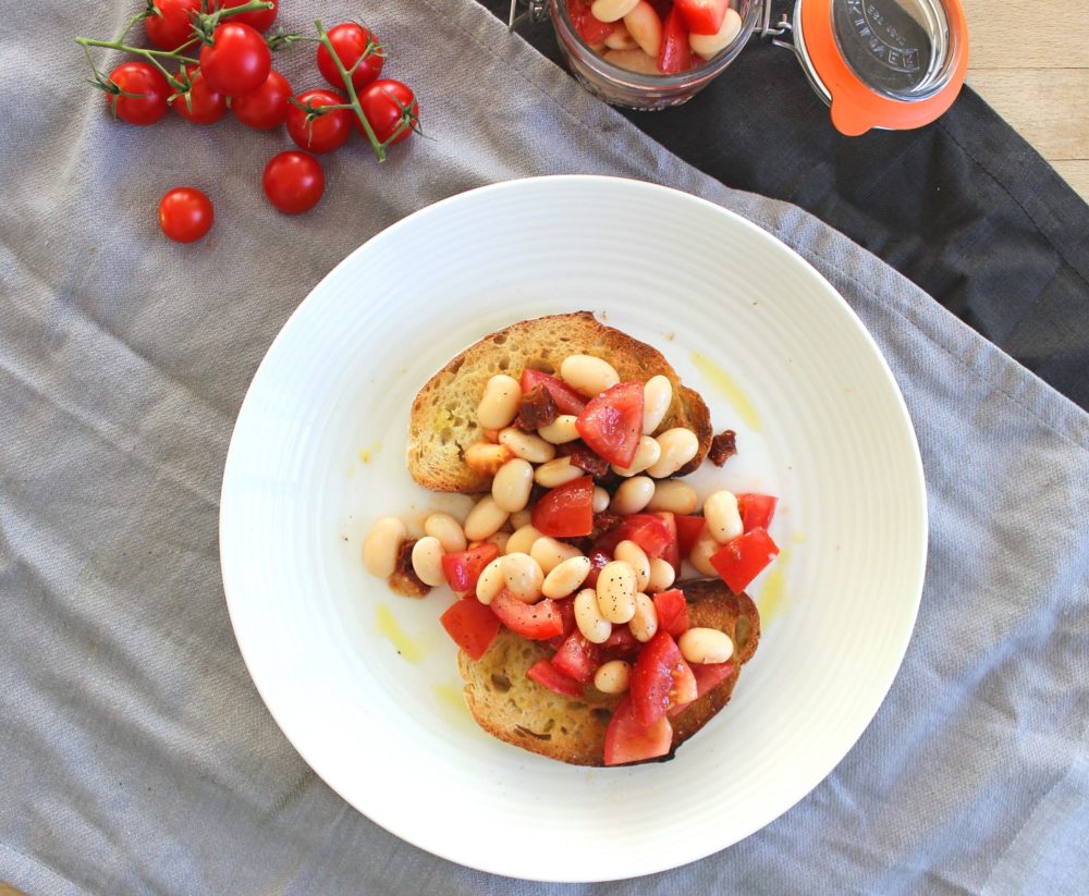 butterbean bruschetta on a white plate next to tomatoes