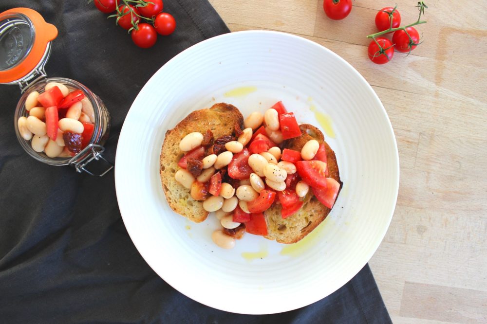 butterbean bruschetta on a white plate next to tomatoes