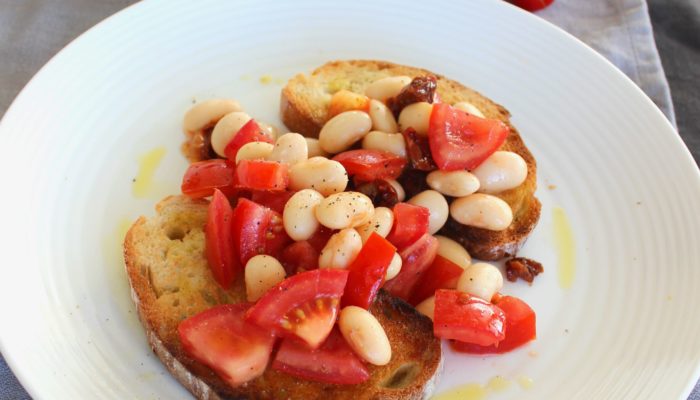 butterbean bruschetta on a white plate next to tomatoes