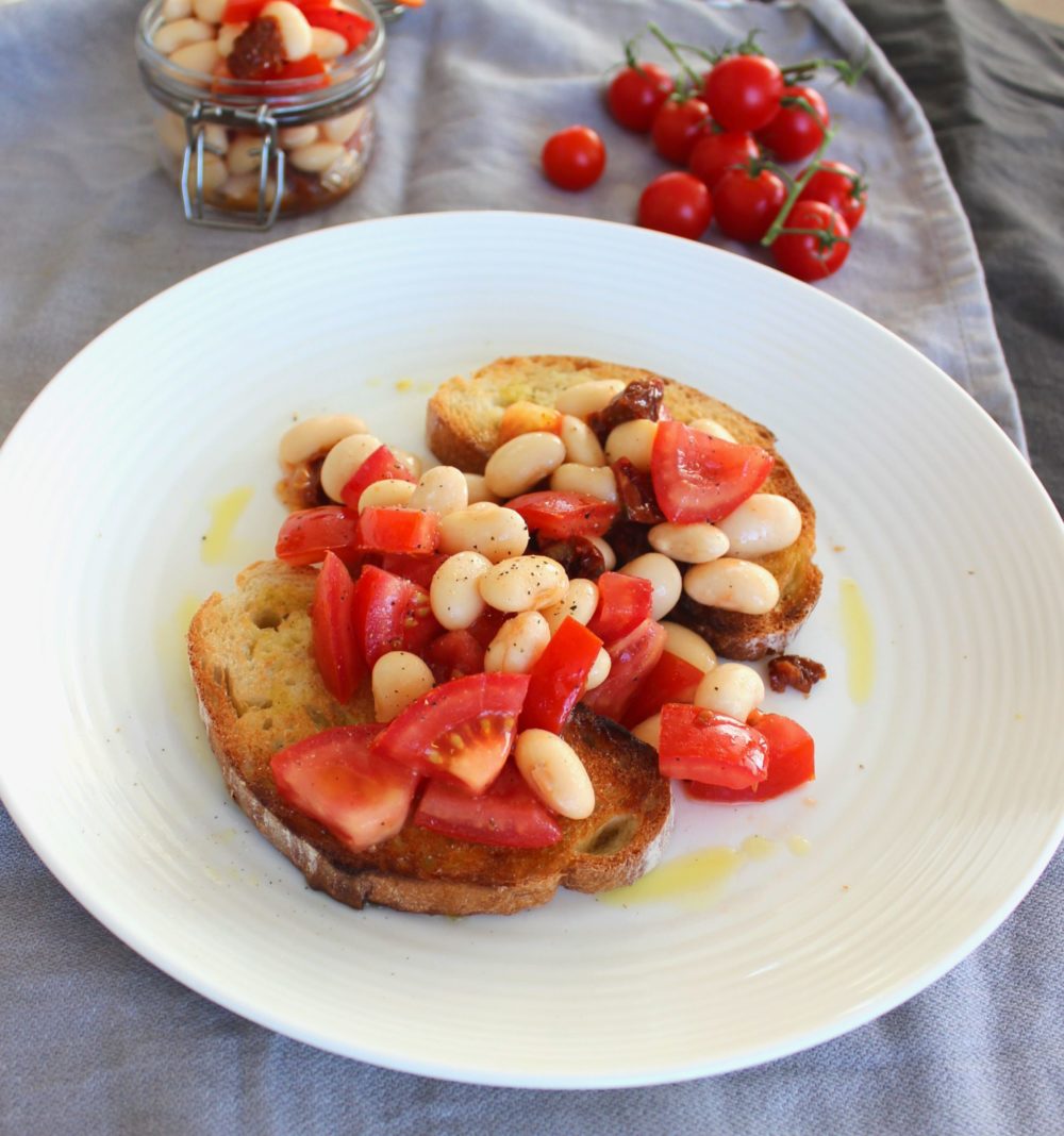 butterbean bruschetta on a white plate next to tomatoes