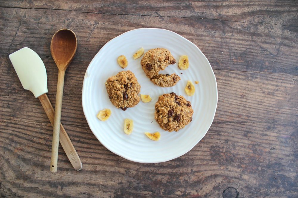 banana chocolate chip oatmeal cookies on a white plate with a spoon and spatula on the side