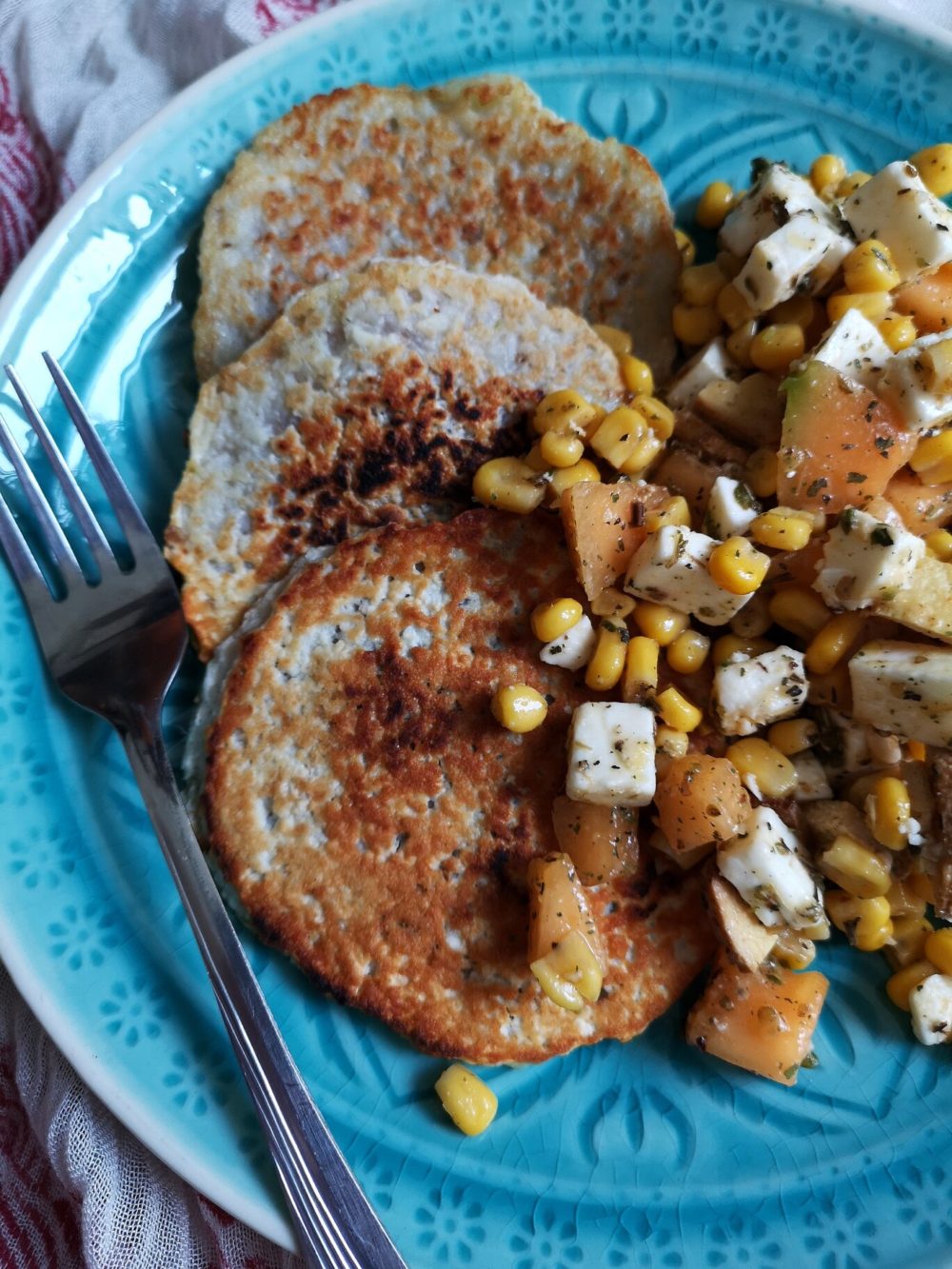 grilled melon and corn salad on a blue plate with a fork against a patterned background