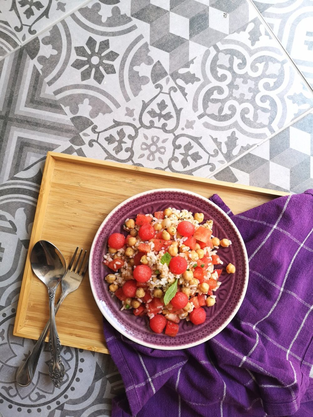 watermelon rice salad on a purple plate with silverware on a tray