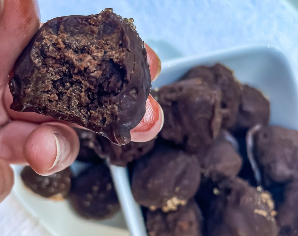 a hand holding a bitten truffle with truffles in the background