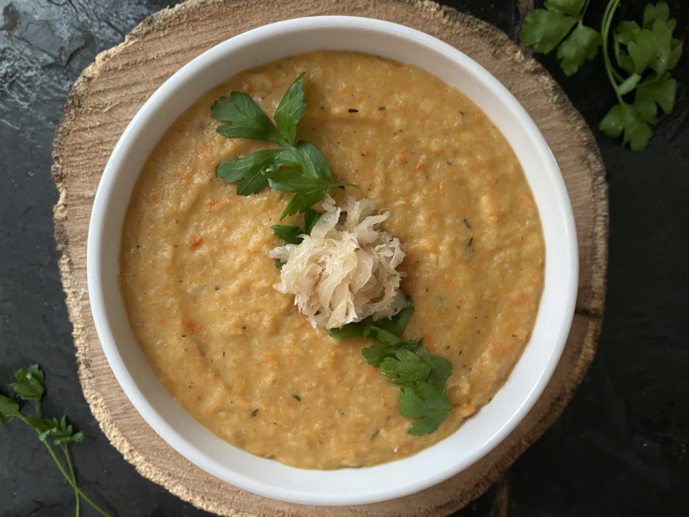 potato sauerkraut soup in a white bowl with a brown and black background