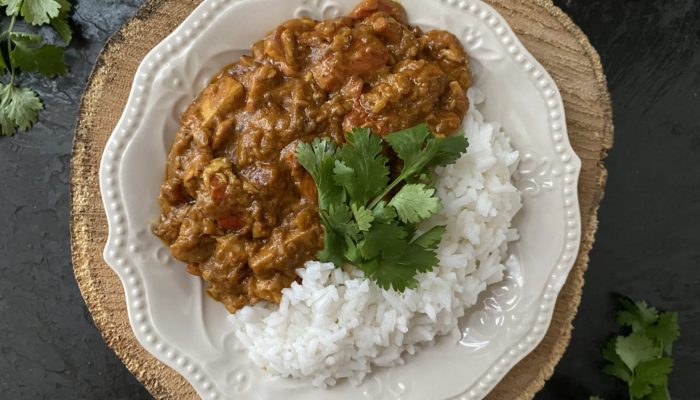 vegan butter chicken of the woods with rice on a white plate against a brown and black background