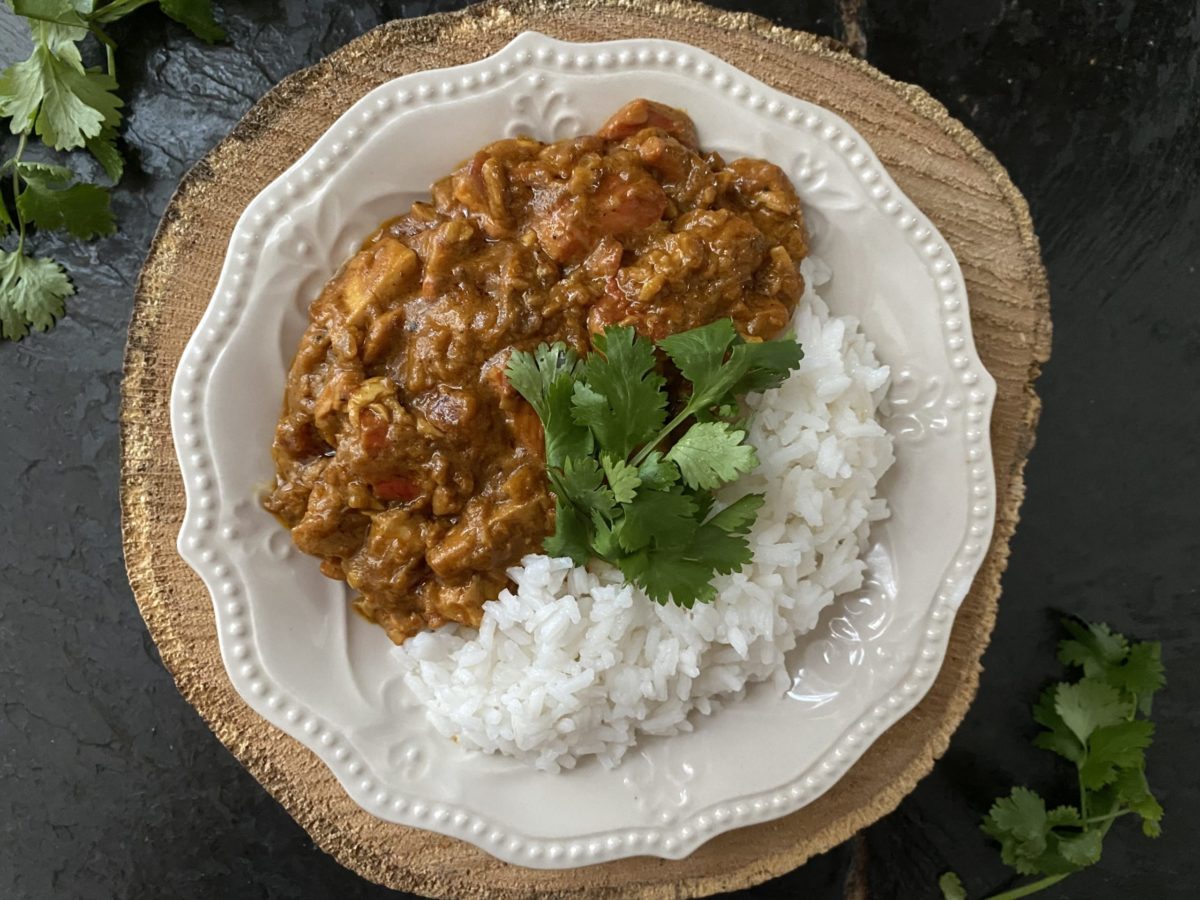 vegan butter chicken of the woods with rice on a white plate against a brown and black background