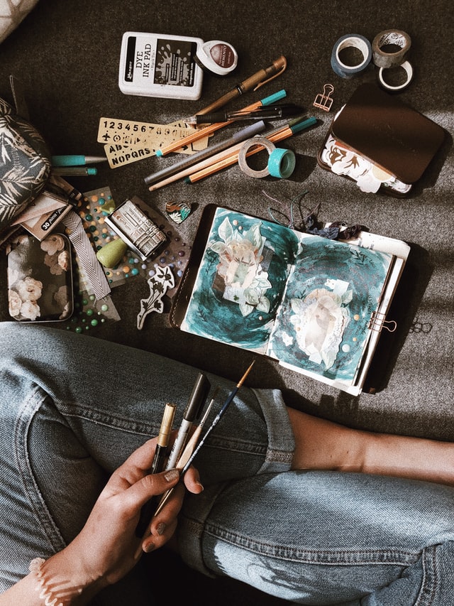 Person sitting with various art tools and a drawing notebook