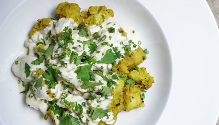 aloo gobi with cashew cream in a white dish against a white background