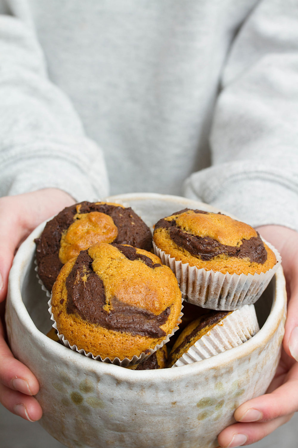 two hands holding vegan pumpkin chocolate marble muffins in a dish