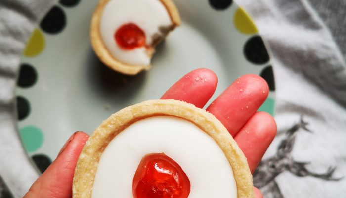 a hand holding a mini cherry tart above a decorative plate