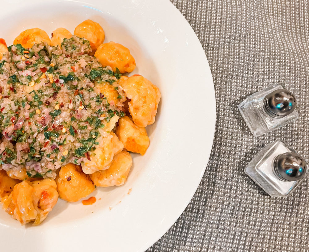 butternut squash gnocchi with chimichurri topping on a white plate next to salt and pepper shakers
