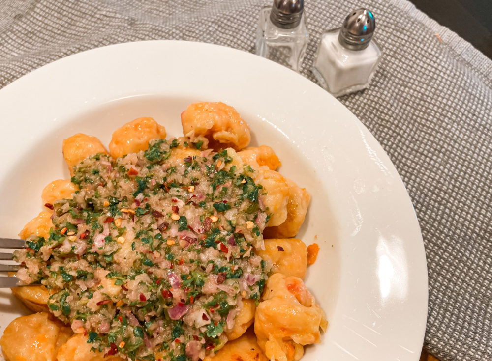 butternut squash gnocchi with chimichurri topping on a white plate with a fork next to salt and pepper shakers