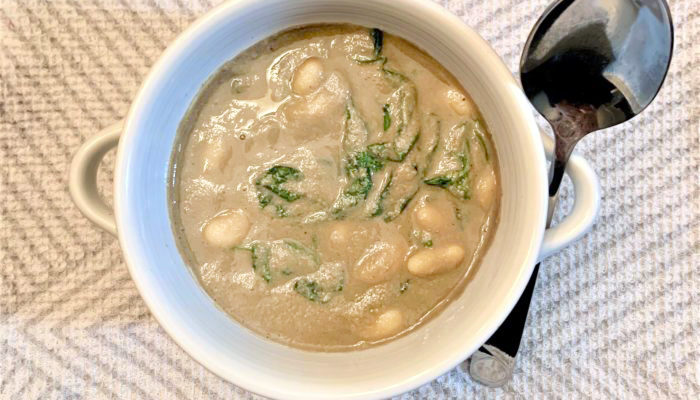 cannellini spinach mushroom soup in a white dish with a spoon