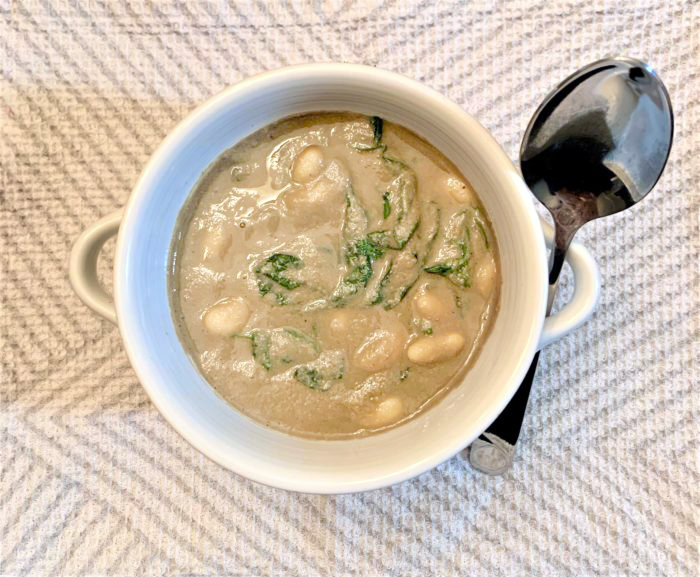 cannellini spinach mushroom soup in a white dish with a spoon