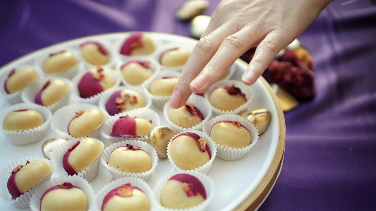 a hand reaching toward raw handmade chocolates on a plate