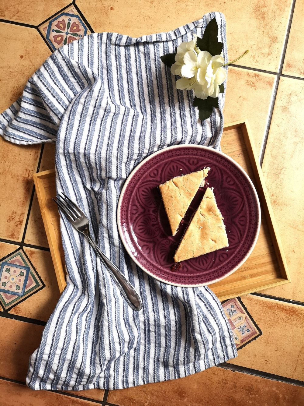 sour cherry pie on a plate with a fork next to a white flower