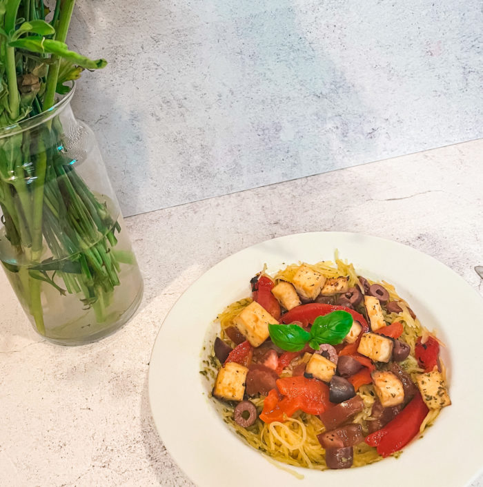 vegan spaghetti squash bowl next to greens in a vase