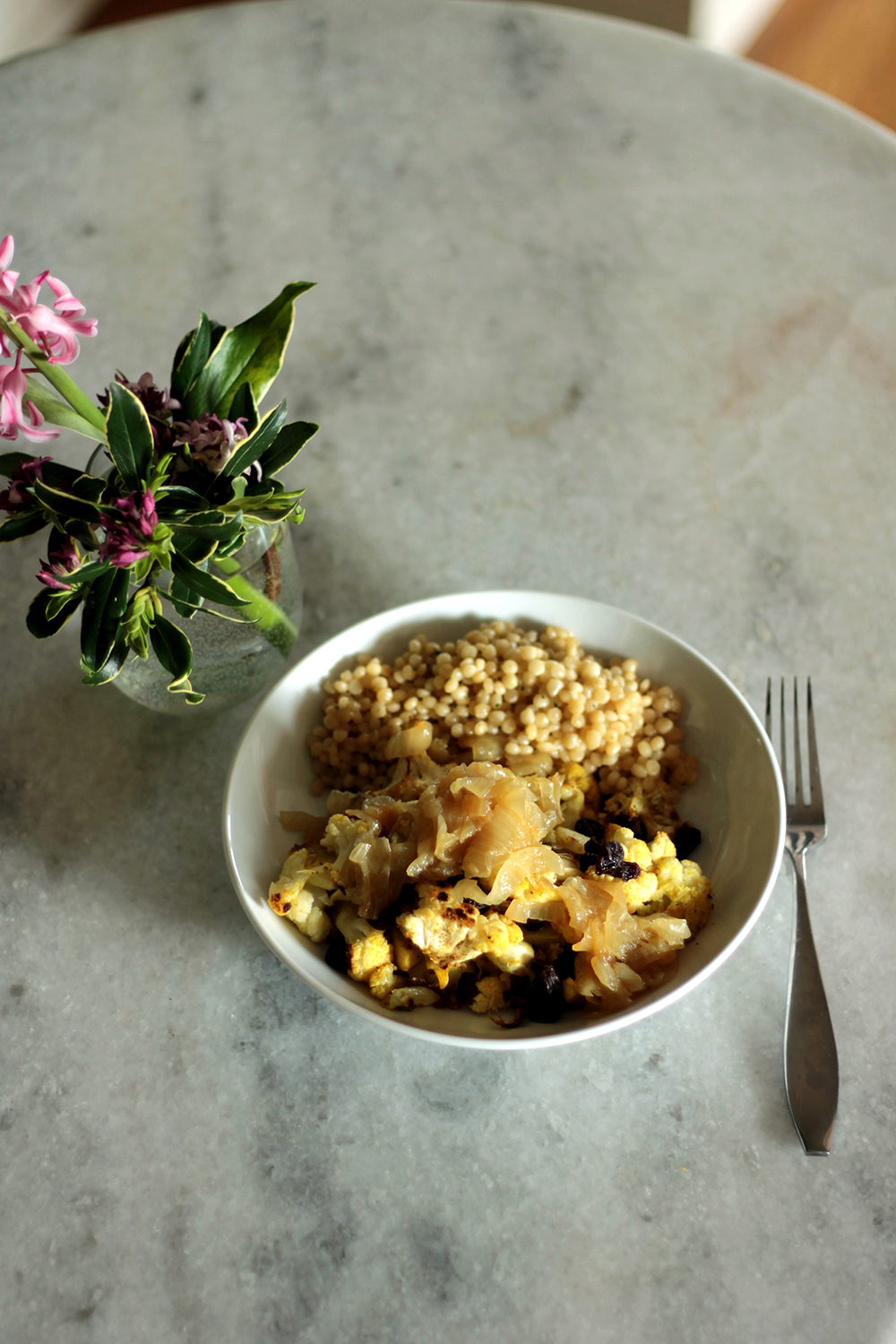 lebanese cauliflower in a white dish next to a fork and a vase with flowers