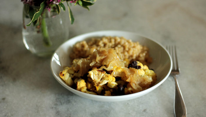 lebanese cauliflower in a white dish next to a fork and a vase with flowers