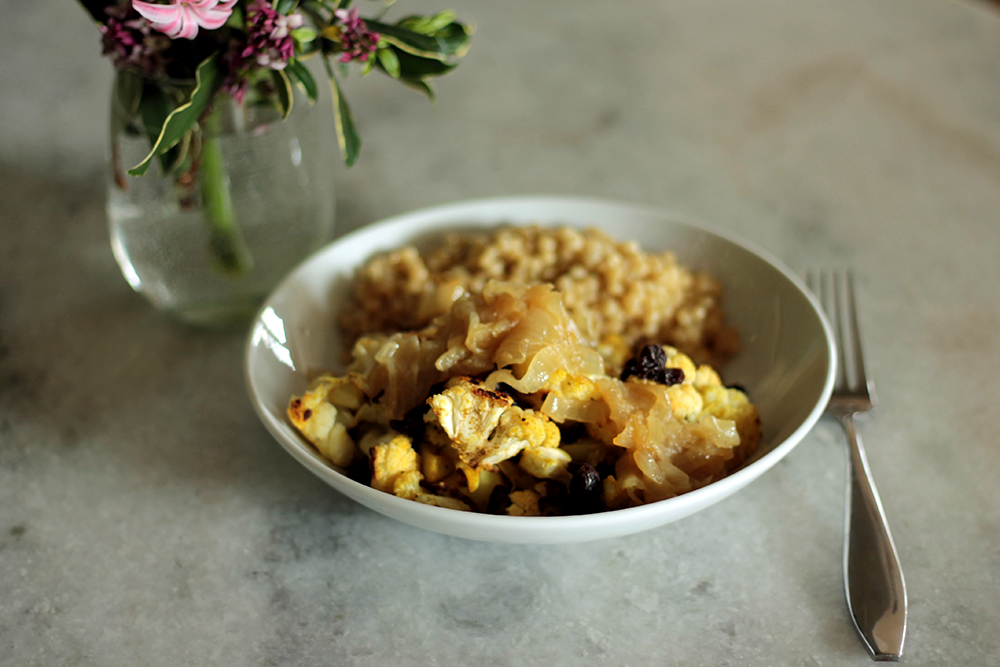 lebanese cauliflower in a white dish next to a fork and a vase with flowers