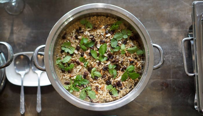mushroom sorghum pilaf in a rilver pot next to silverware on a table