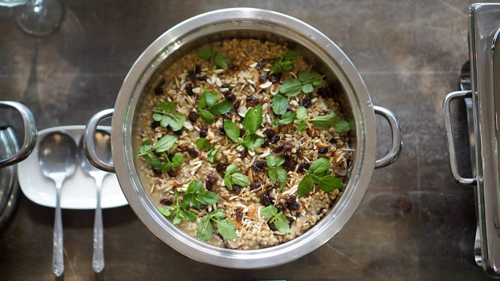 mushroom sorghum pilaf in a rilver pot next to silverware on a table