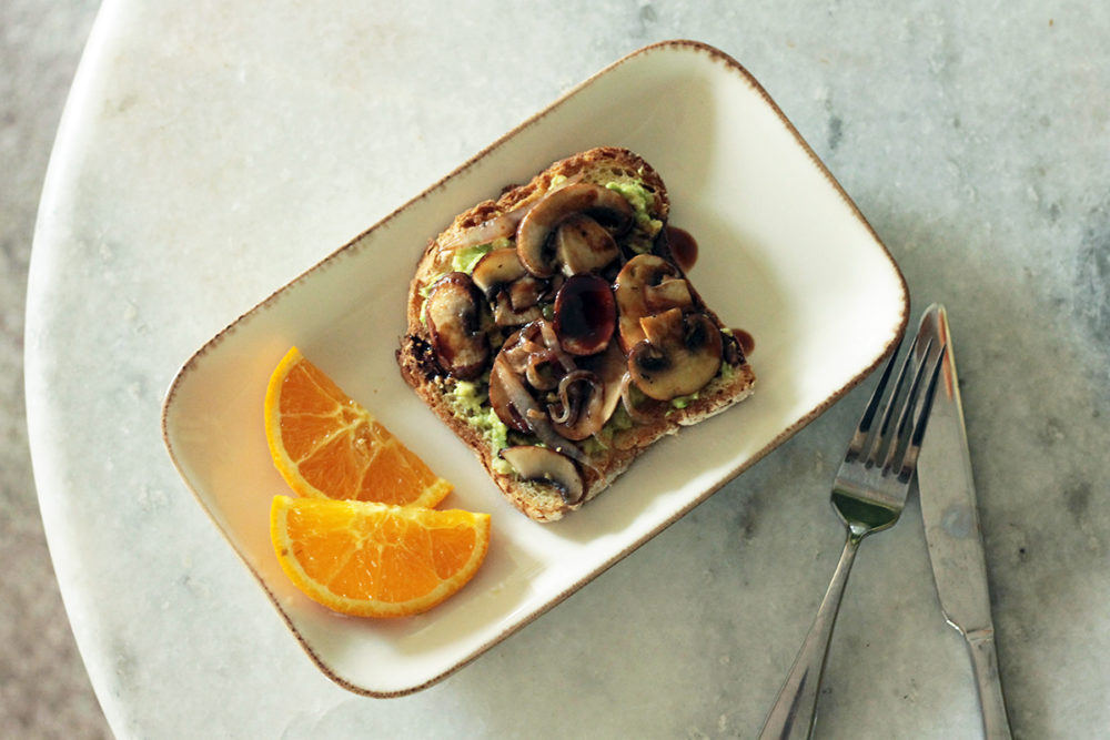 avocado toast on a plate next to orange slices and silverware on a table