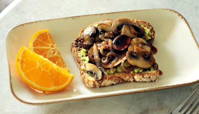 avocado toast on a plate next to orange slices