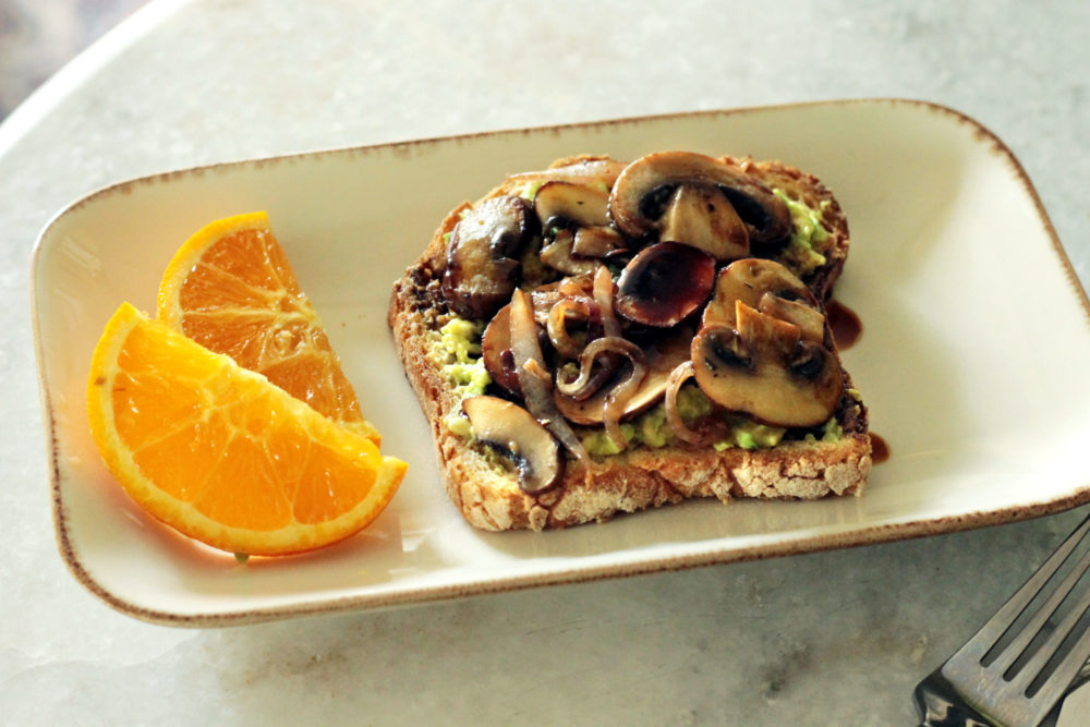 avocado toast on a plate next to orange slices