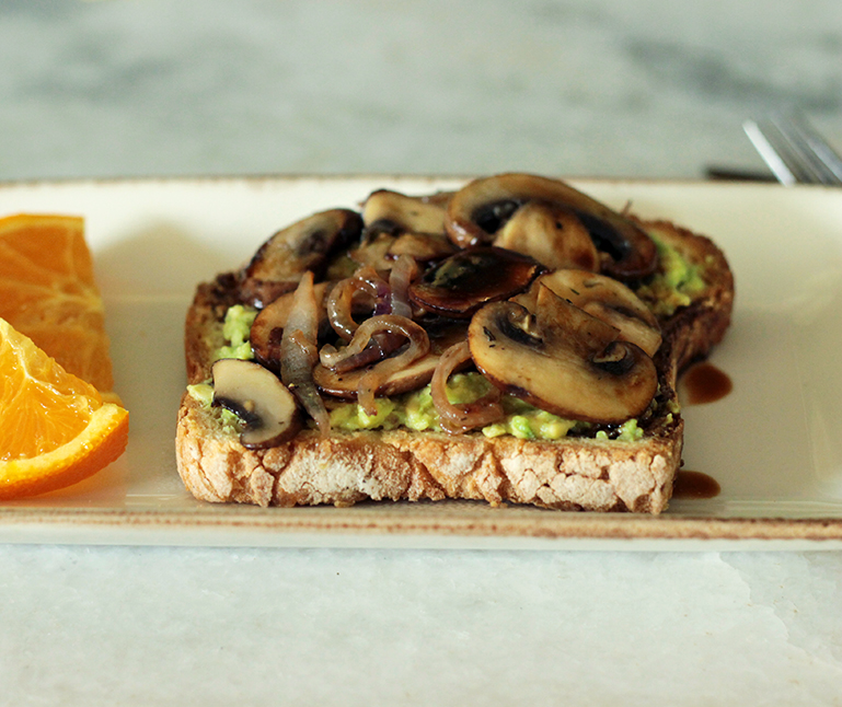 avocado toast on a plate next to orange slices