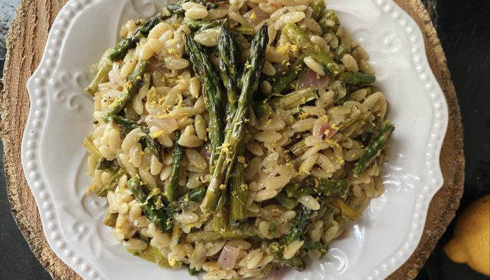 lemon asparagus orzo on a white plate with brown and black background