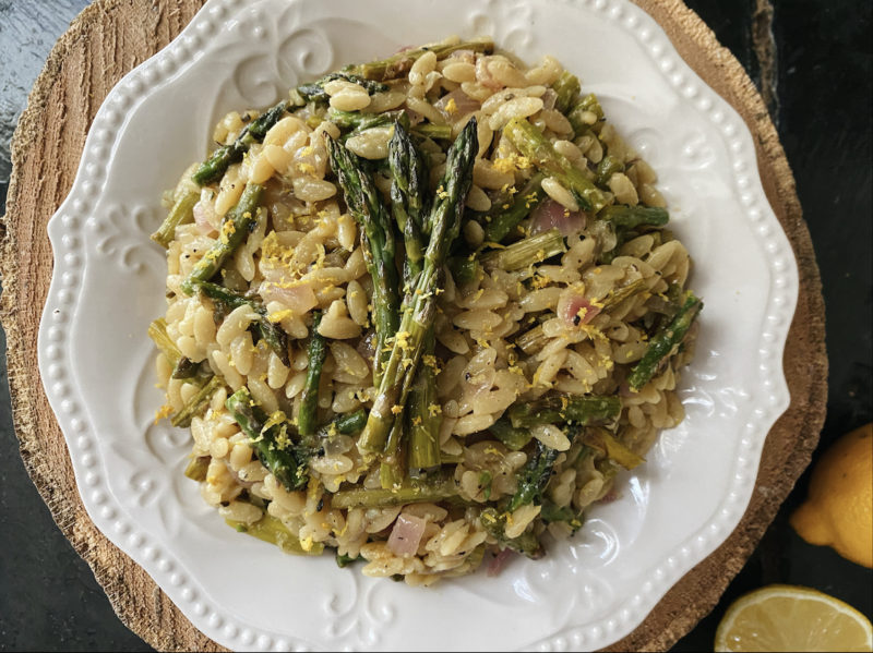 lemon asparagus orzo on a white plate with brown and black background