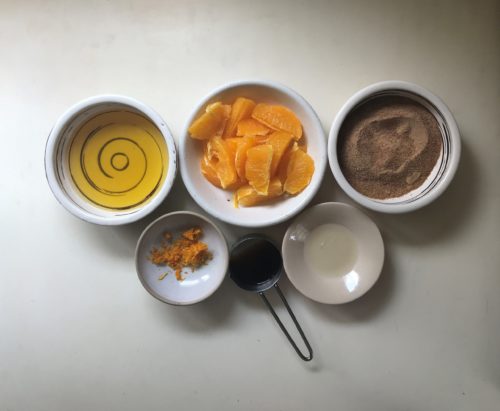 ingredients for sweet potato cake: orange, orange juice, coconut sugar, orange zest and coconut oil, on a white surface